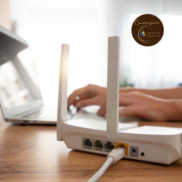 Un routeur Wi-Fi blanc moderne sur une table en bois avec une personne travaillant sur un ordinateur portable en arrière-plan flou.