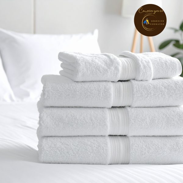 Pile de serviettes de bain blanches propres et moelleuses posées sur un lit blanc dans une chambre lumineuse.