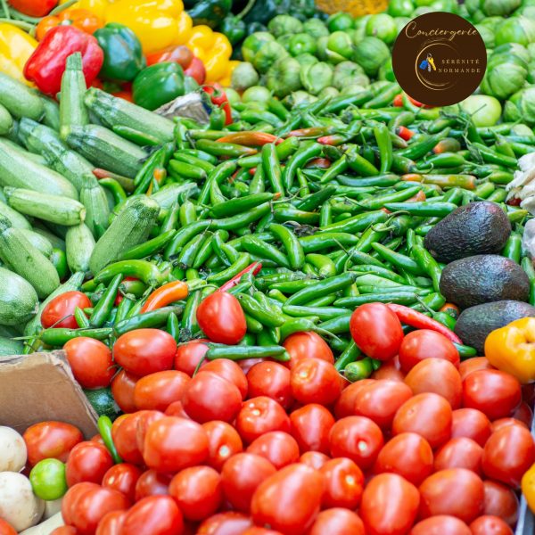 Étal coloré sur un marché avec une abondance de tomates rouges, piments verts, poivrons jaunes, courgettes et avocats.