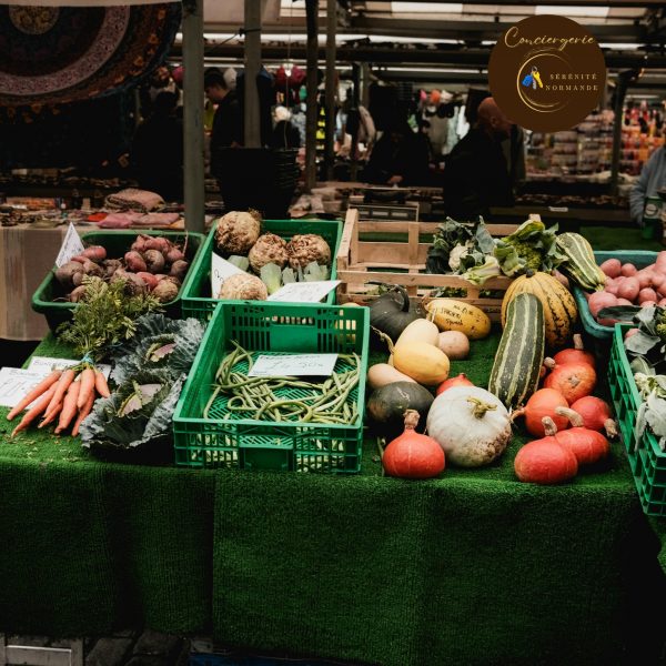 Étal de marché couvert présentant des légumes frais en Normandie : courgettes, potirons, carottes et haricots verts dans des cagettes.