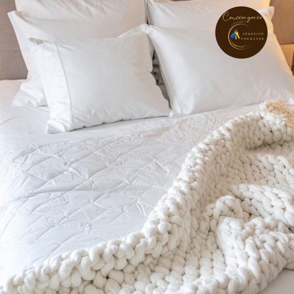 Lit double fait avec des draps blancs impeccables, de gros oreillers et un plaid douillet en grosse maille écrue.